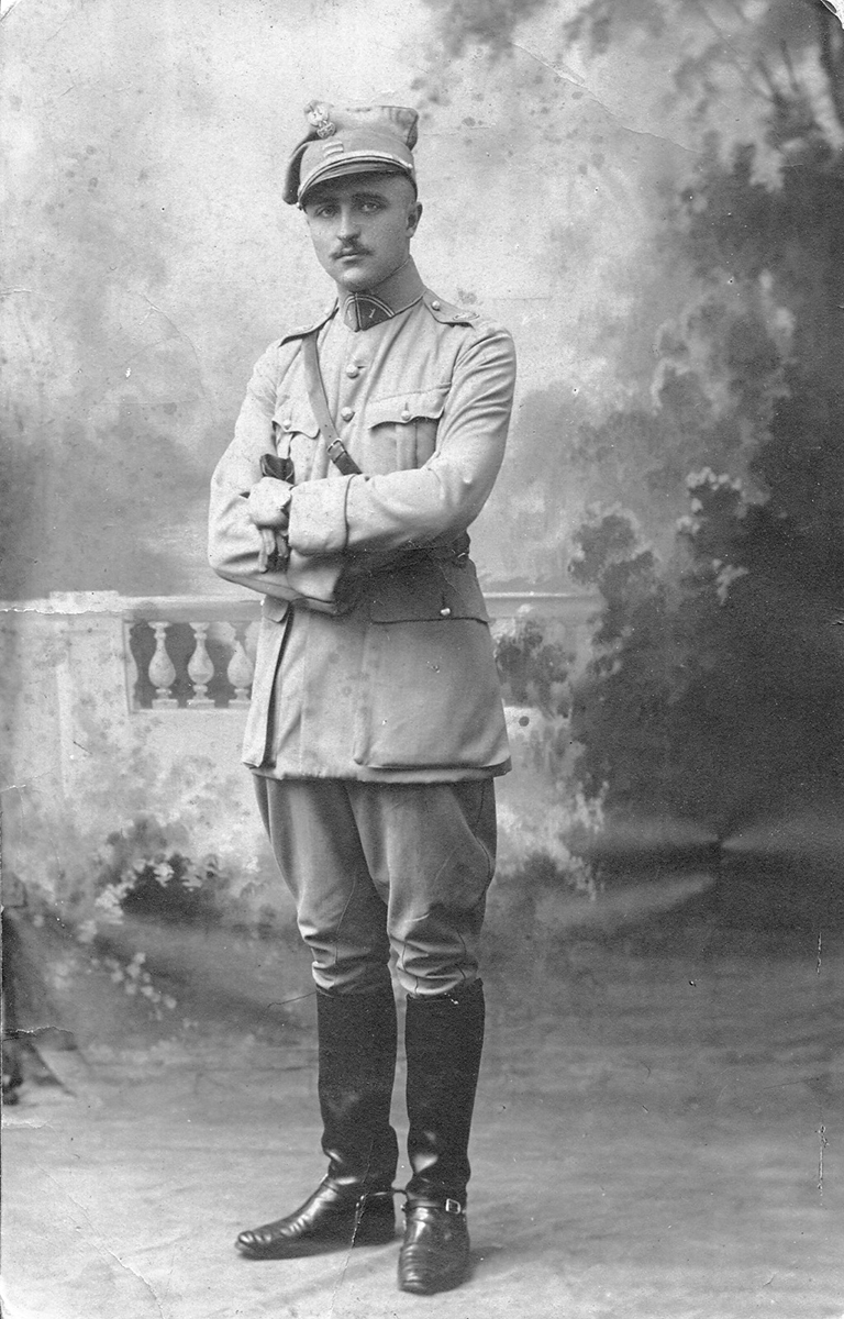 Fotografia archiwalna czarno-biała, zrobiona około 1919 roku, przedstawia młodego mężczyznę ujętego w całej postaci. Ubrany jest w mundur Błękitnej Armii generała Hallera. Mężczyzna pozuje na tle fotograficznym z fragmentem balustrady i roślinnością