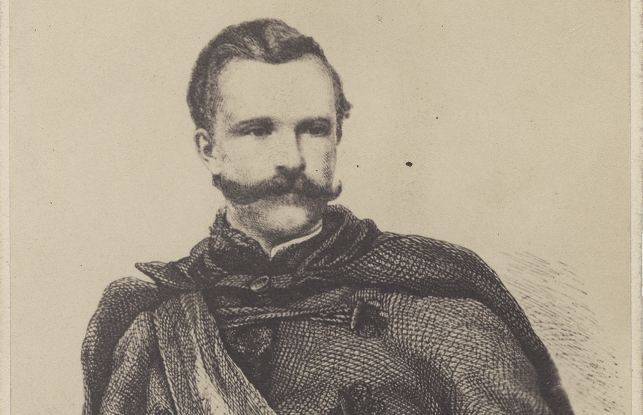 Fotografia archiwalna, czarno-biała, przedstawiająca mężczyznę z bujnym wąsem, ubranego w mundur powstańczy z 1863 roku, w ujęciu do bioder, z głową lekko zwróconą w prawo, tło neutralne.
