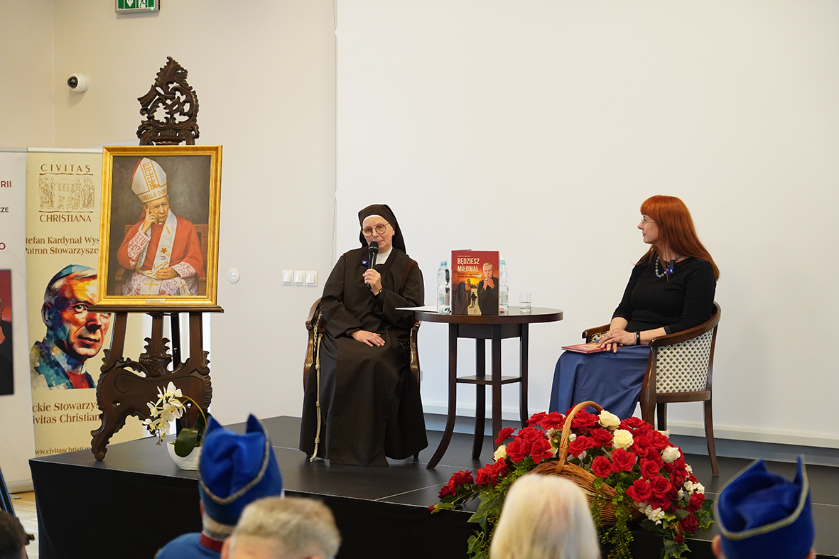 Msza święta we wnętrzu kaplicy pałacowej. Przy marmurowym ołtarzu stoi ksiądz w złotej szacie liturgicznej i unosi ręce. Przed nim leży długi, czerwony dywan. Po obu stronach dywanu stoją wierni.